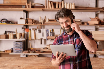 Wall Mural - Carpenter using a mobile phone and holding digital tablet