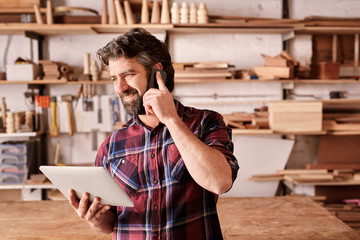 Wall Mural - Small business owner in workshop with phone and digital tablet