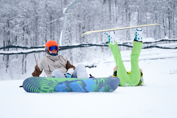 Two snowboarders - men and women sitting in the mountains