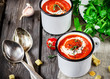 Tomato cream soup in mugs and greens on a wooden table.