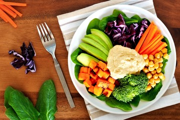 Wall Mural - Healthy lunch bowl with avocado, hummus and fresh vegetables, overhead scene on wooden table