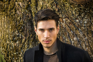 handsome young man leaning against tree