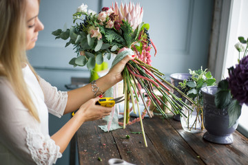 Florist at work: pretty young blond woman making fashion modern bouquet of different flowers