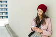 © Westend61 - Young woman leaning against concrete wall looking at cell phone