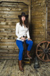 © dmitrypk - the girl cowboy sitting on wooden background wall in the hands of a gun