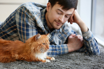 Wall Mural - Young man with fluffy cat lying on a carpet