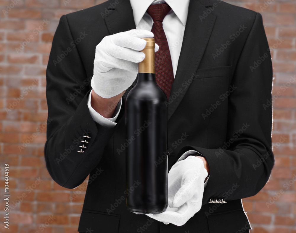 Man holding a bottle of red wine in hands on brick wall background