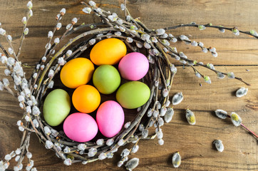 Easter background, selective focus. Homemade hand painted colorful easter eggs in nest from willow branches close-up over retro wooden rustic background