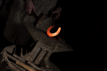 Wall Mural - The blacksmith forging glowing horseshoe with hammer on the anvil in smithy