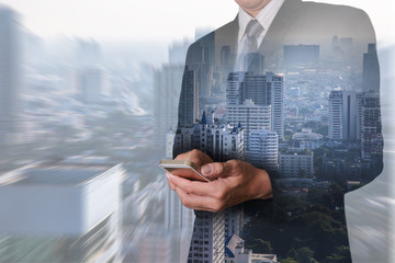 Double exposure of business man hand touch screen smart phone, mobile and city in a foggy morning as communication concept.