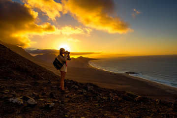 Beautiful seascape view on Cofete coastline with young female traveler on the sunset on Fuerteventura island in Spain. General plan with a lot of space