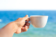 coffee cup in a female hand with a sea view