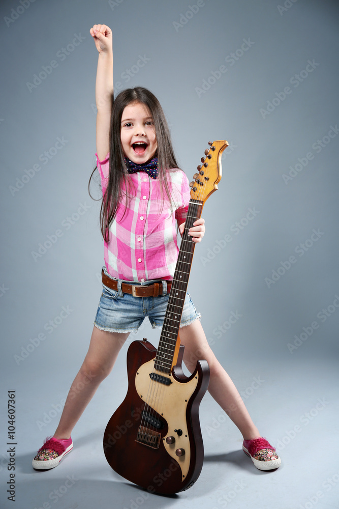 Beautiful artistic little girl playing guitar on grey background
