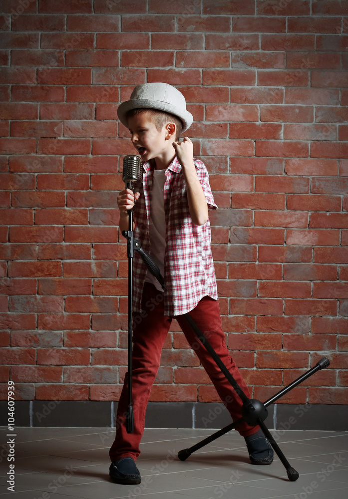 Little boy singing with microphone on a brick wall background