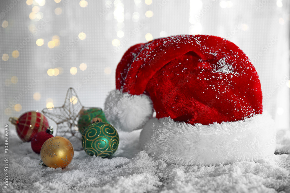Santa Claus hat with toys on a snowy table over glitter background