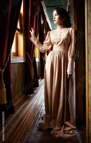 Young woman in beige vintage dress of early 20th century standin