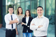 © bokan - Portrait of smiling young and successful business team. Focus on confident young businessman standing in front of his coworkers.