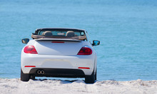 White Convertible Automobile With The Top Down At The Beach On A Sunny Day With A Soft Blue Water Background