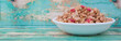 Breakfast cereal with dried raspberry fruit pieces in white bowl over wooden background