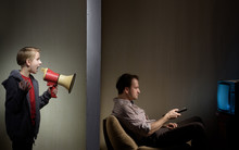 Man Watching TV While His Son Calling Him Through A Megaphone. Lack Of Father's Attention Concept