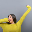 Portrait of young woman stretching and yawning against gray back