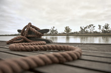 Rope Tied To A Mooring Cleat On A Floating Wooden Dock On The River.