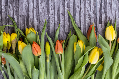 Fototapeta do kuchni Wiosenny bukiet kwiatów z żółtych i czerwonych tulipanów oraz żonkili na szarym tle z motywem muru i cegły