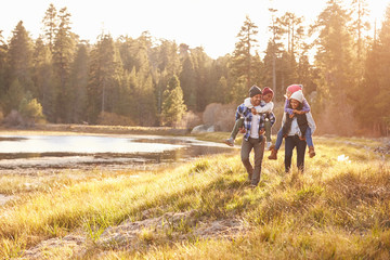 Wall Mural - Parents Giving Children Piggyback Ride On Walk By Lake