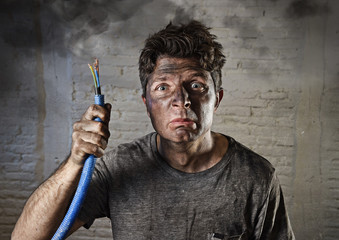 young man holding cable smoking after electrical accident with dirty burnt face in funny sad express