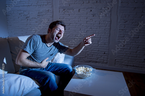 Fotografia, Obraz young television addict man sitting on home sofa watching TV and eating popcorn