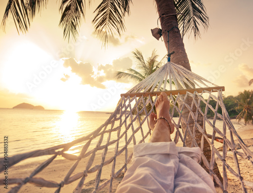 Fotomural Female legs in a hammock on a background of the sea, palm trees and sunset