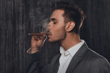 Wall Mural - Side view of a cheeky man in suit on the grey background smoking