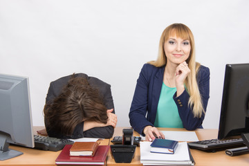  The situation in office - frustrated woman lay on the table, her colleague happily looks into the frame