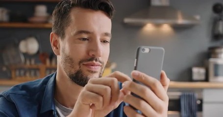 Attractive man at home using smart phone in kitchen sending message on social media