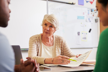 Wall Mural - Senior teacher at desk talking to adult education students