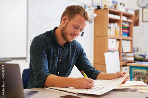 Fotografía Young bearded male teacher at desk marking students’ work
