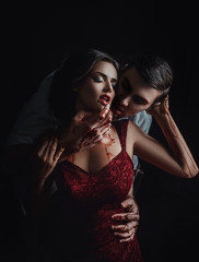 Sexy girl vampire in passionate embrace man's hands, dripping drop blood, man hugging woman. red dress. Two people, couple in love. Gothic bloody passion. Glamour classic halloween image