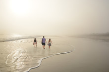 Family Walking On Beautiful Foggy Beach At Sunrise . Reflection Of The Sun In The Water. Large Copy Space. Daytona Beach, Florida, USA.
