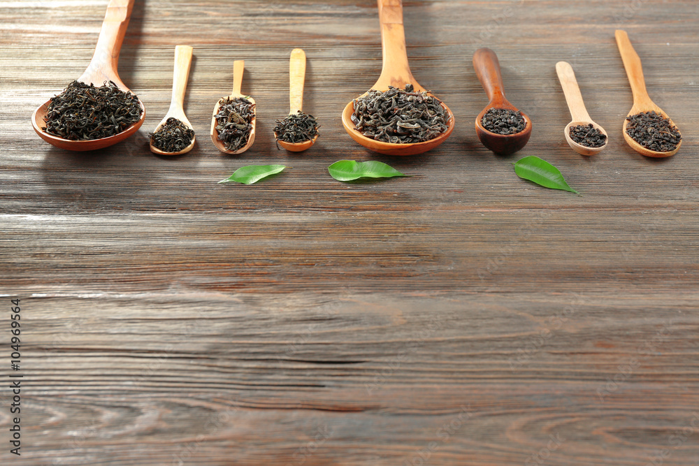 Dry tea with green leaves in wooden spoons on table background, copy space