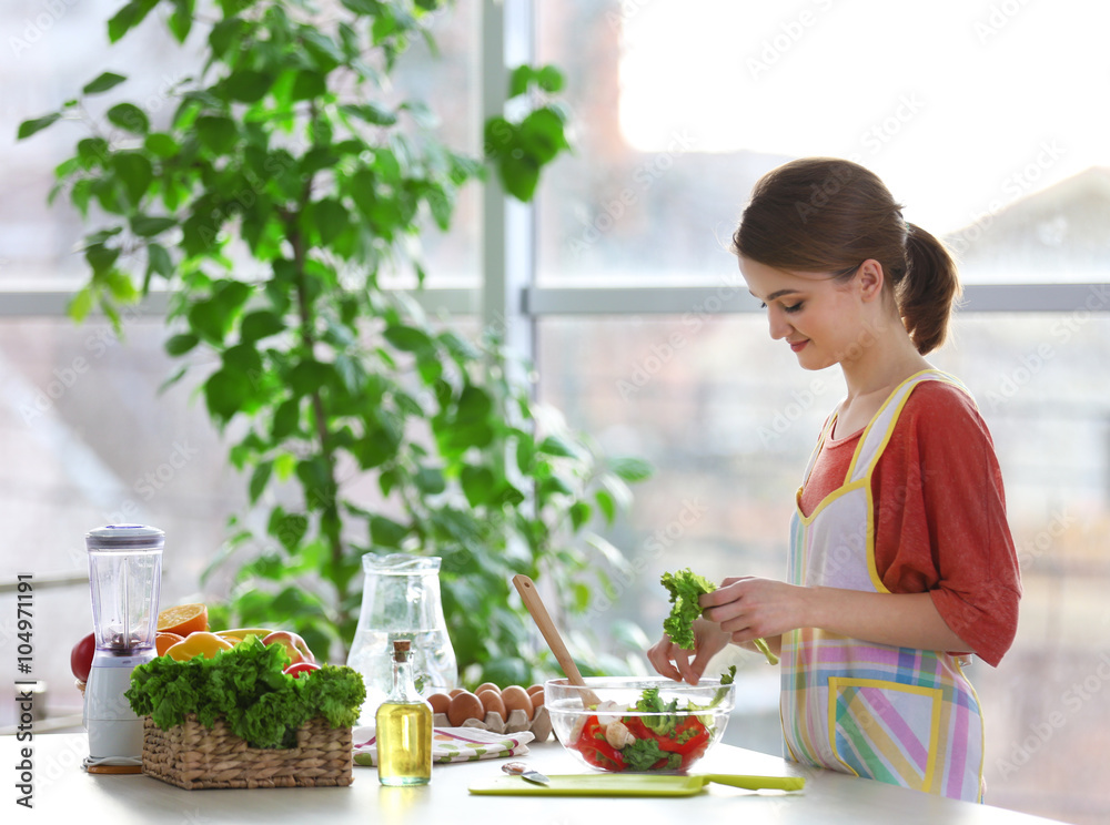 Young woman preparing vegetable salad in the kitchen