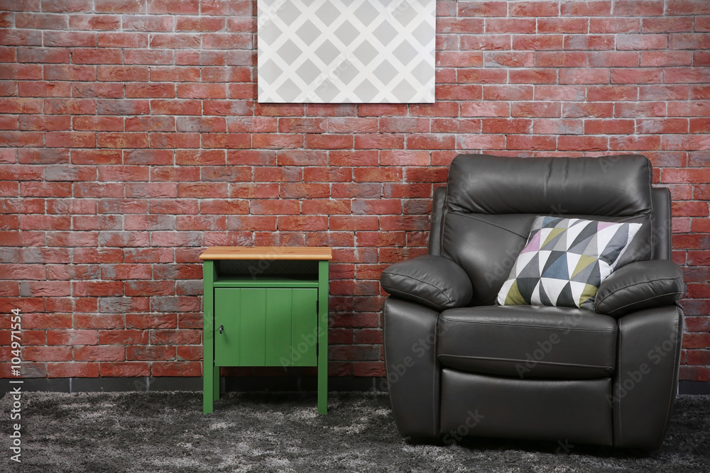 Brown leather armchair and green small table against brick wall background