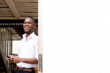 Black man standing next to white wall with mobile phone