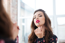 Seductive woman applying red lipstick to lips looking in mirror