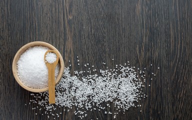 A wooden bowl of salt crystals on a wooden background