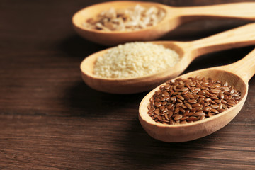 Sesame, flax and sunflower seeds in wooden spoons on table, closeup