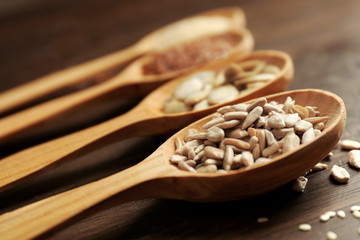 Wall Mural - Sesame, flax, pumpkin and sunflower seeds in wooden spoons on table, closeup