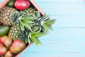 Box of tropical fruits in box over blue table