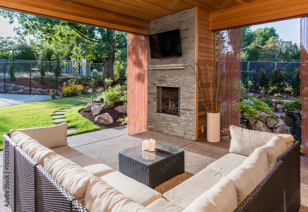 Beautiful covered patio outside new luxury home with television, fireplace, and lush green yard - obrazy, fototapety, plakaty 