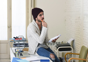 young trendy businessman in cool hipster beanie and informal look writing on pad working thoughtful