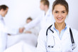 © rogerphoto - Female doctor smiling on the background with patient in the bed and two doctors